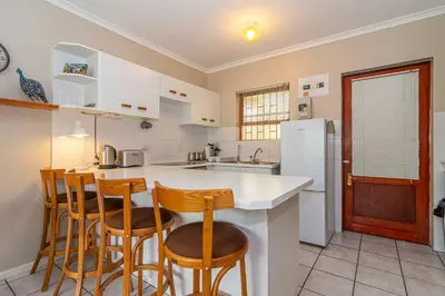 a kitchen with a white counter and wooden bar stools at Oak Terrace 28 in Hermanus
