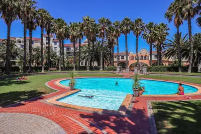 a pool with palm trees and people swimming in it at 107 St Tropez Eyrie Holiday Apartments in Cape Town
