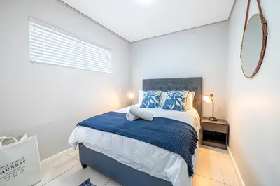 a bedroom with a bed with a blue blanket and a mirror at Top Floor Beachfront w Views, Blouberg, 51 Beach Break in Bloubergstrand
