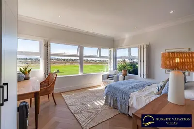 a bedroom with a bed and a desk and windows at Sunsets Jasmine Villa in Cape Town