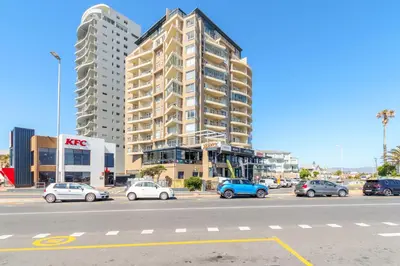a parking lot with cars parked in front of a building at Wake Up to the Waves - Portico in Cape Town