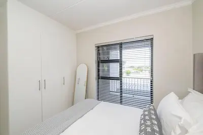 a white bedroom with a bed and a window at Cozy Apartment in Brackenfell, Cape Town, ZA in Brackenfell