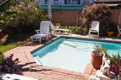 a swimming pool with two lawn chairs and two chairs at Luxurious Flatlet in the heart of Mowbray in Cape Town