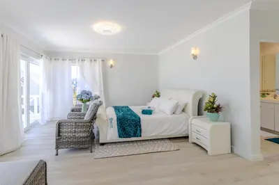 a white bedroom with a bed and a chair at Hermanus - Heart of the Sea in Hermanus