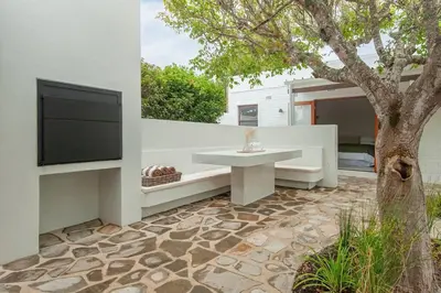 a patio with a table and a tv and a tree at Heartwood Cottage in Hermanus