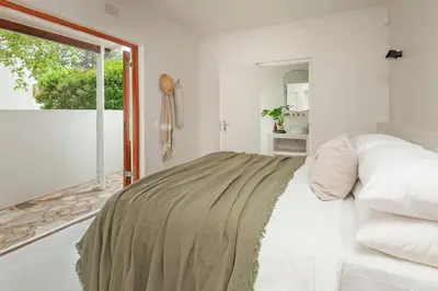 a white bedroom with a bed and a window at Heartwood Cottage in Hermanus
