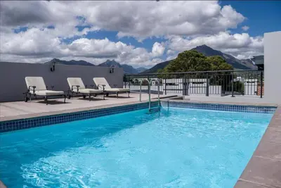 a swimming pool with chairs and mountains in the background at 23 On The Den Studio Apartment in Stellenbosch