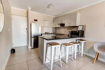 a kitchen with a counter with stools and a refrigerator at Beachside Getaway in Cape Town