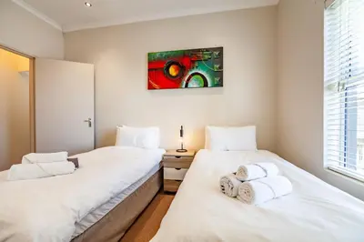 two beds in a room with white sheets at Coral Breeze Walk to Everything in Cape Town