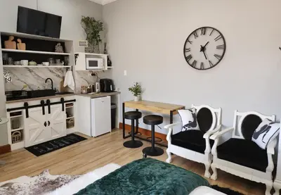 a living room with a table and a clock on the wall at Le Graan Guestroom in Malmesbury