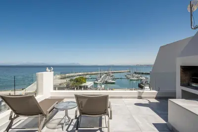 a balcony with chairs and a view of a marina at 34 Gordonia, Beachfront Penthouse in Gordonʼs Bay