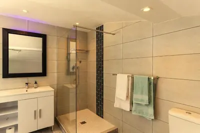 a bathroom with a shower with a sink and a mirror at Bikini Beach Townhouse in Gordonʼs Bay