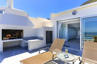 a patio with a fireplace and a table and chairs at Bikini Beach Townhouse in Gordonʼs Bay