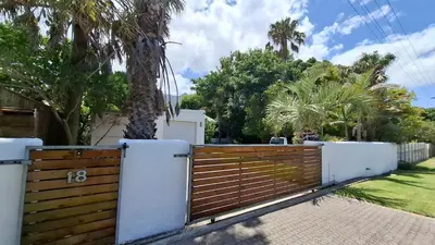 a wooden fence in front of a house with palm trees at Coco Cabana in Kleinmond