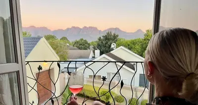 a woman holding a glass of wine looking out a window at Serenity Suite in Somerset West