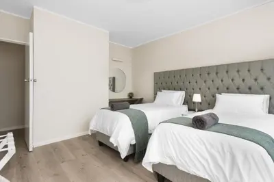 a bedroom with two beds and a tufted headboard at ZenDen Destinations' Seaside Sanctuary Suite in Strand