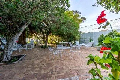 a patio with chairs and tables and a tree at ZenDen Destinations' Seaside Sanctuary Suite in Strand