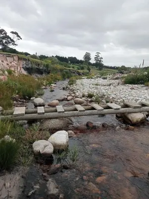 a bridge over a river with rocks in a field at 3 Jongens Villa in Voëlklip