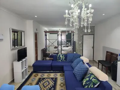 a living room with a blue couch and a chandelier at Tia Maria bachelor apartment in Cape Town