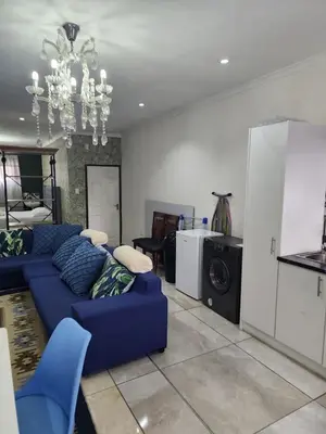 a living room with a blue couch and a kitchen at Tia Maria bachelor apartment in Cape Town