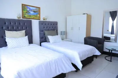 a bedroom with two beds and a chair at paradise guest house in Cape Town