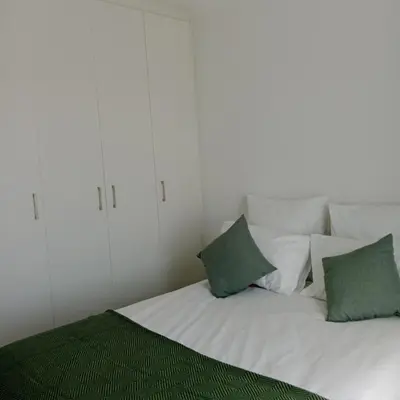 a white bed with two green pillows on it at The Cozy Nest in Cape Town