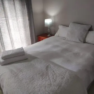 a large white bed with a lamp and a window at Johannies Home at Panorama Hospital in Cape Town