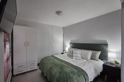 a bedroom with a large bed with white walls at Peppertree Place in Cape Town