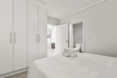 a white bedroom with a teddy bear sitting on a bed at Waters Edge Luxury Apartment Century City in Cape Town
