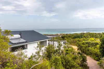 a house on a hill with the ocean in the background at SeaScape Silversands in Bettyʼs Bay