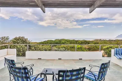 a patio with chairs and a table and a view of the ocean at SeaScape Silversands in Bettyʼs Bay