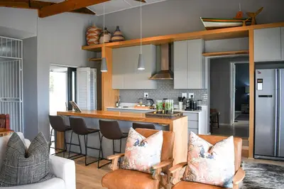 a kitchen with white cabinets and a bar with chairs at MOS-Palmiet 72 in Kleinmond