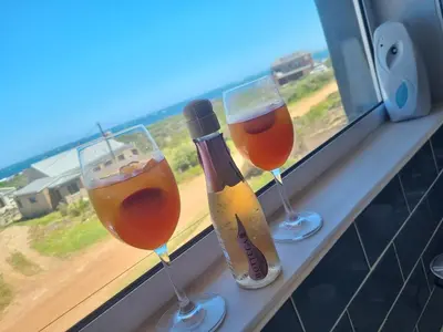 three wine glasses and a bottle on a window sill at OceansCrest Seaview Apartment in Bettyʼs Bay