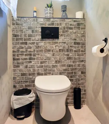 a bathroom with a white toilet and a brick wall at Tide's whisper in Hermanus