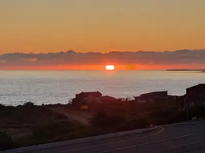a sunset over the water with a road and houses at La Mer in Bettyʼs Bay
