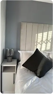 a white bed with a black pillow next to a nightstand at Malithabo in Khayelitsha