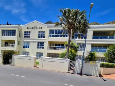 a building with a palm tree in front of a street at 'Goldwater on Beach' - 3 Bedroom Beachfront with Balcony & BBQ - Sleeps 6 in Gordonʼs Bay