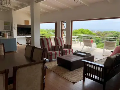 a living room with chairs and a table and a balcony at Onrus Home with a Sea View in Hermanus