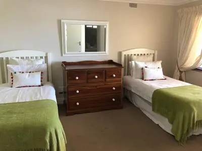 a bedroom with two beds and a dresser and a mirror at Onrus Home with a Sea View in Hermanus
