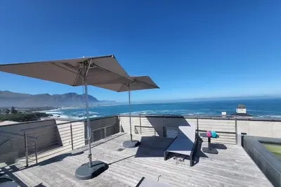 a patio with an umbrella and chairs and the ocean at Whale Watchers studio in Hermanus