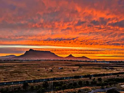 a sunset with a train in a field with mountains at Luxury Three Bedroom Axis- Ocean and Mountain Views in Cape Town
