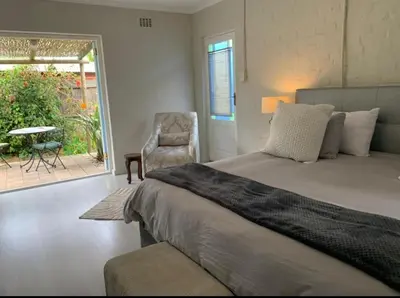 a bedroom with a bed and a chair and a patio at Crinum House and cottages in Bloubergstrand in Cape Town