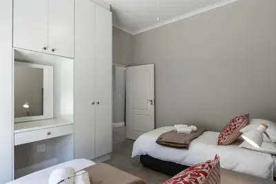 a white bedroom with two beds and a mirror at Twelve on Arum in Somerset West
