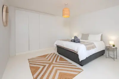 a white bedroom with a bed and a rug at Fun in the Voelklip Sun in Hermanus