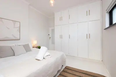a white bedroom with white cabinets and a bed at Fun in the Voelklip Sun in Hermanus