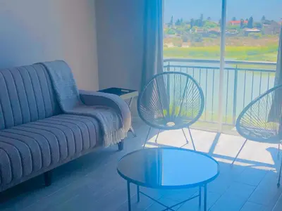 a living room with a couch and two tables and a balcony at Loft apartment by the lake in Cape Town