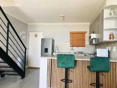 a kitchen with a counter and two green chairs at Loft apartment by the lake in Cape Town