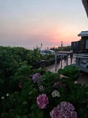 a garden with flowers and a table with a sunset in the background at La Mer Seafront Selfcatering Accommodation Kleinmond in Kleinmond
