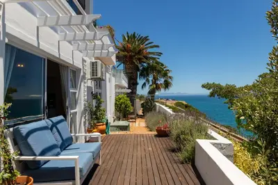 a house with a blue couch on a patio with the ocean at Whale Watchers Gordons Bay in Gordonʼs Bay