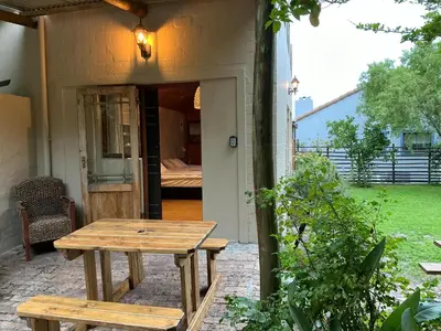 a patio with a wooden table and a bed at Swallows Cottages in Hermanus